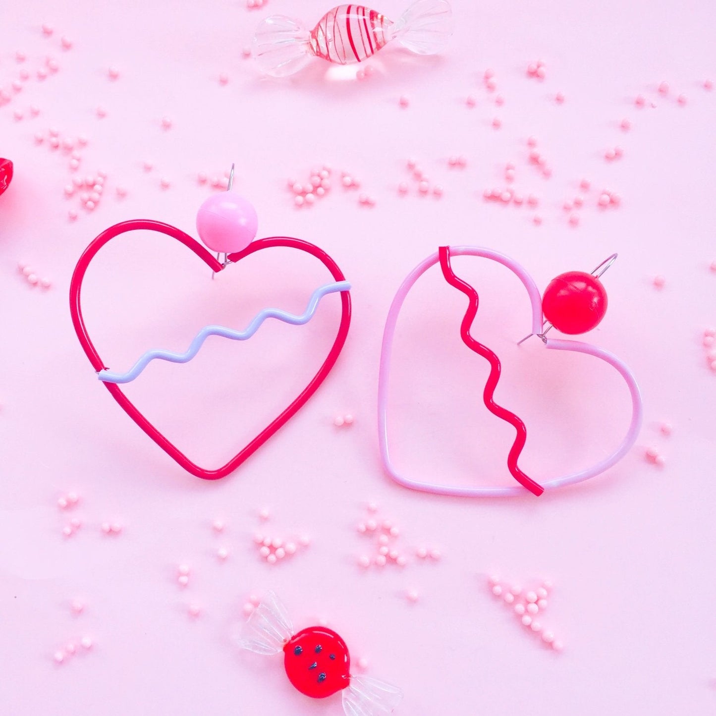 Two heart-shaped earrings on a pink background with candy decorations.