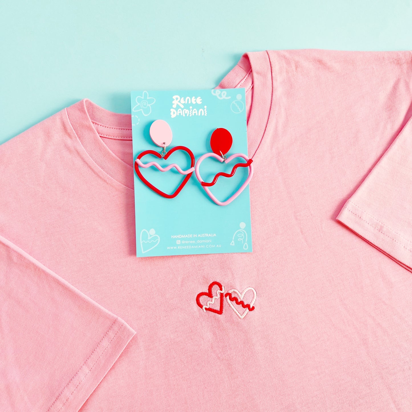 Heart-shaped earrings on a pink shirt with a blue background