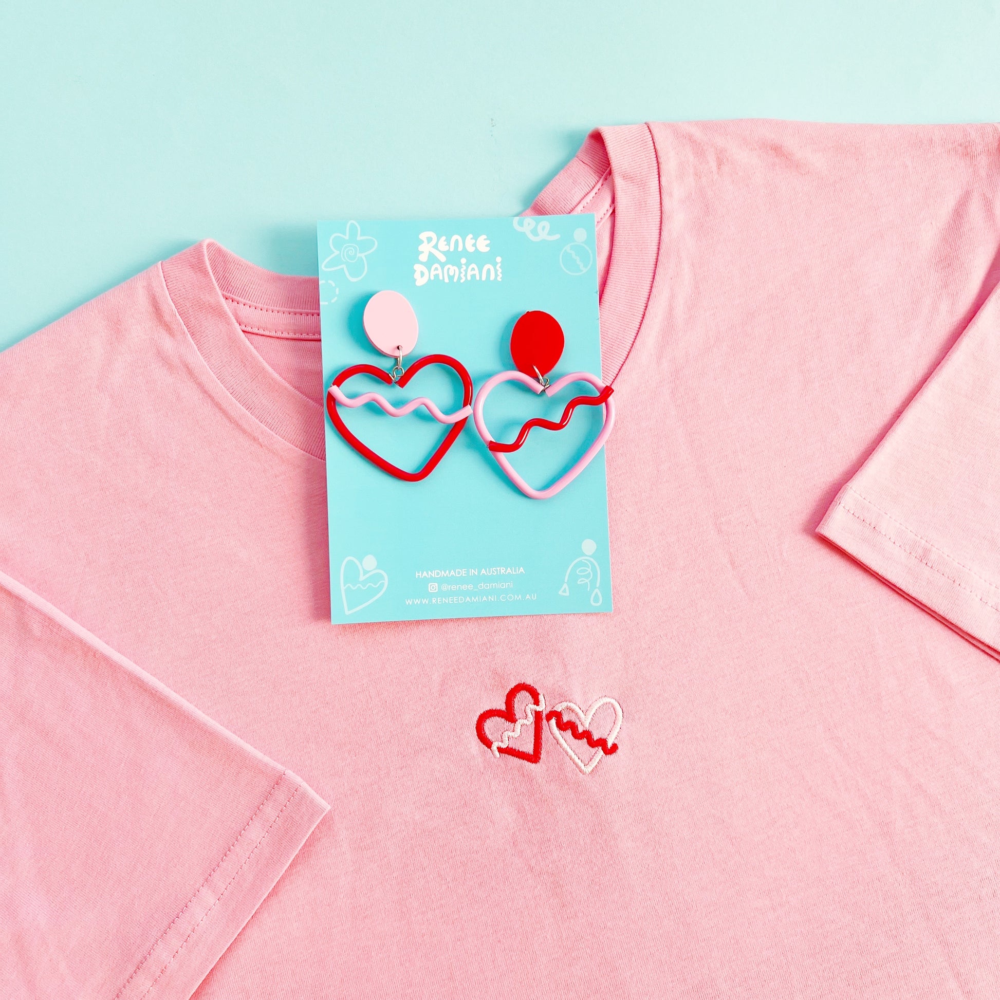 Heart-shaped earrings on a pink shirt with a blue background