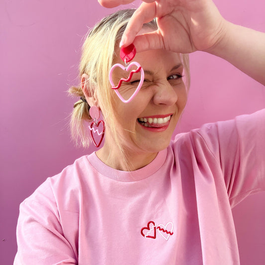 Person wearing pink heart-shaped earrings and a matching shirt against a pink background