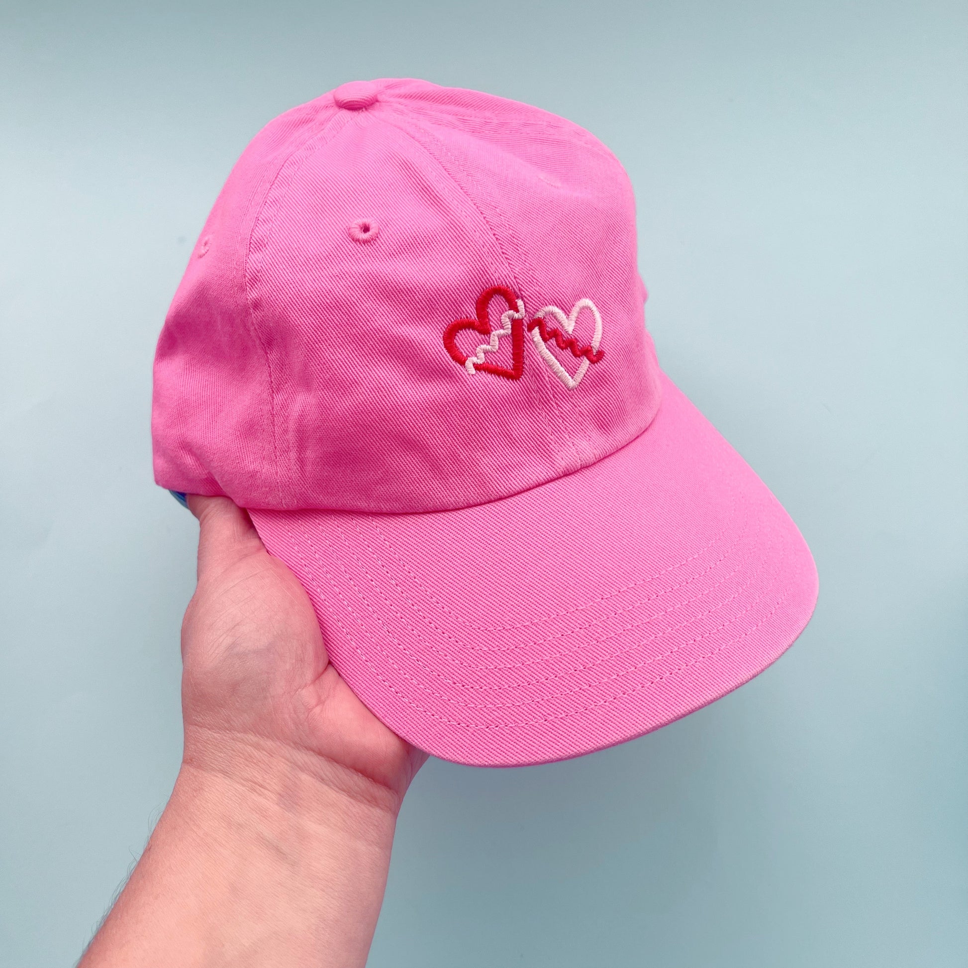 Pink cap with embroidered hearts held against a light gray background