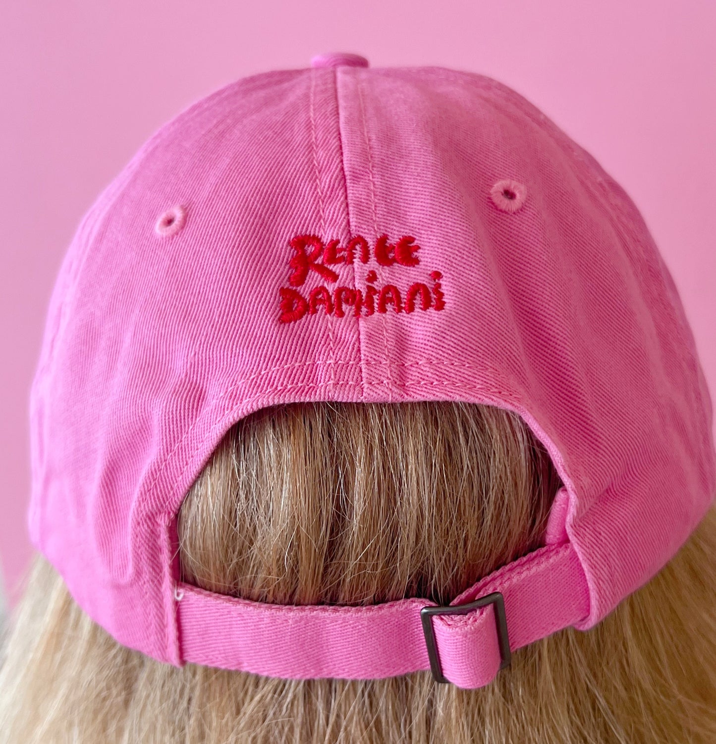 Pink cap with 'Renée Damiiani' logo on a pink background