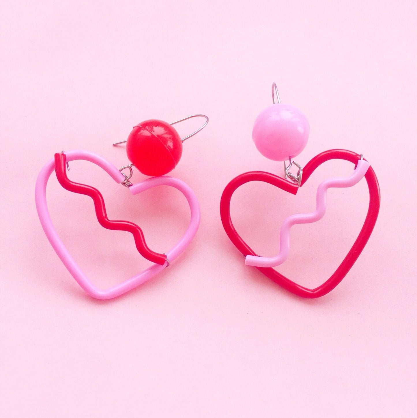 Heart-shaped earrings with pink and red designs on a pink background